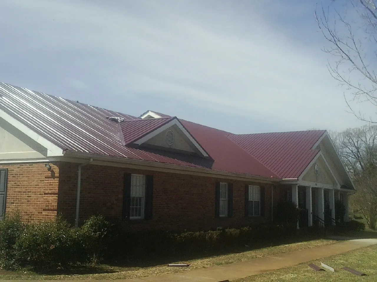 Red metal roof with gabled entries on a long brick building, from a Hail Damage Roof Repair job in Eliot