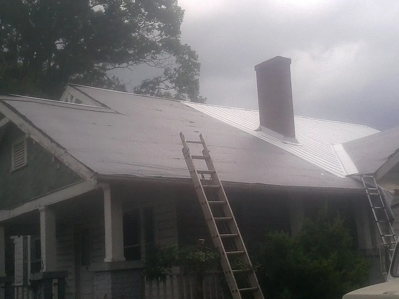 Ladders against a metal roof on an older home with a brick chimney in Eliot