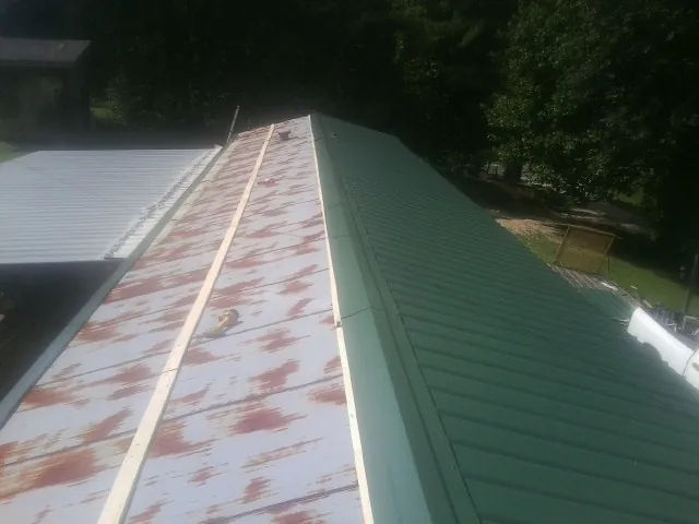 Old rusted panels beside newly installed green metal roofing — Wind Damage Roof Repair by Roofing Brothers in Eliot