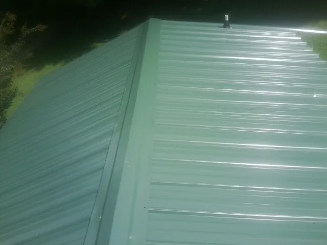 New green metal panels meeting at the ridge of a roof — Flat Roof Repair work by our crew in Eliot